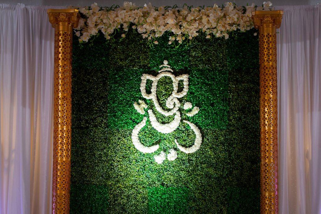 Custom Hindu mandap backdrop Pittsburgh — floral Ganesha on greenery wall with gold pillars, luxury Indian wedding decor